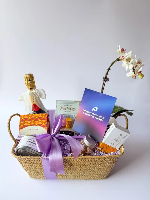 Luxury woven gift basket with sparkling wine, coffee, artisan treats and an orchid, finished with a purple satin ribbon