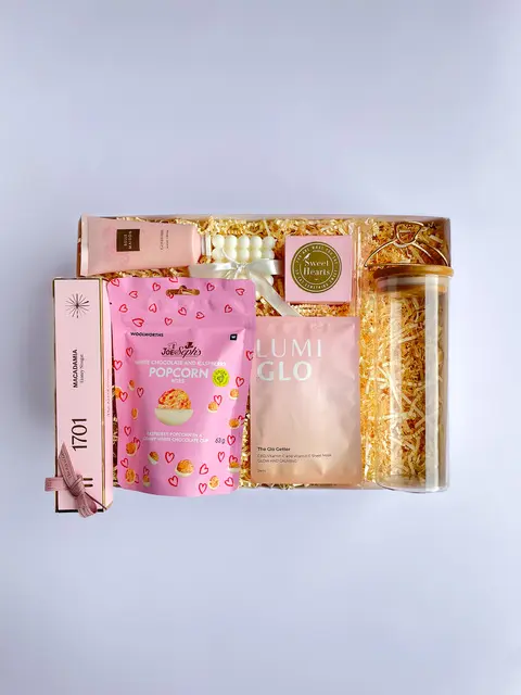 Pink gift box with chocolate popcorn, sweet treats, candle and beauty accessories